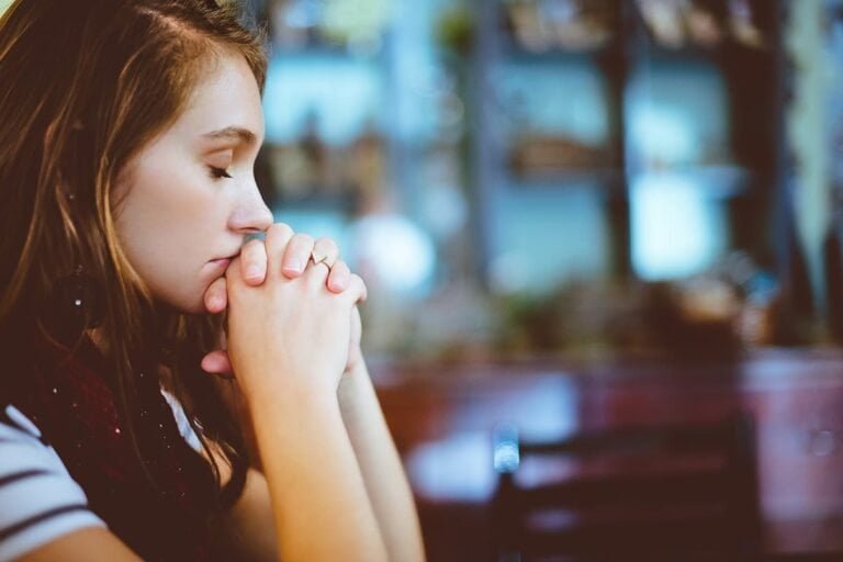 Prayerful woman praying with closed eyes, spiritual reflection, peaceful moment.