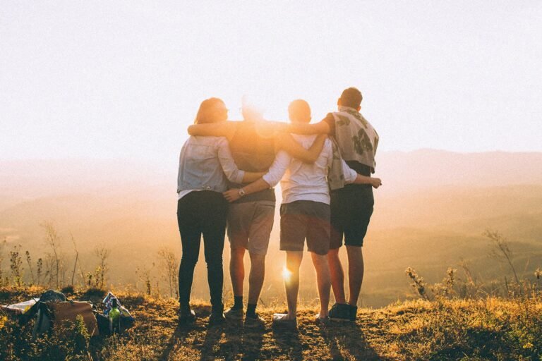 A group of friends standing together at sunset, embracing and enjoying nature.