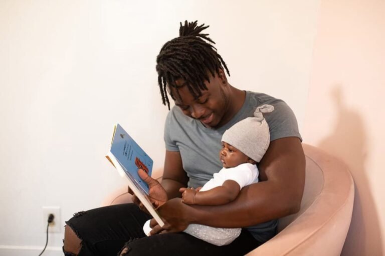 Man reading a book to a baby on a pink sofa, promoting blockchain education.